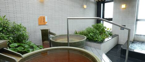 A modern indoor spa area with a large wooden tub, a small fountain, and potted plants.