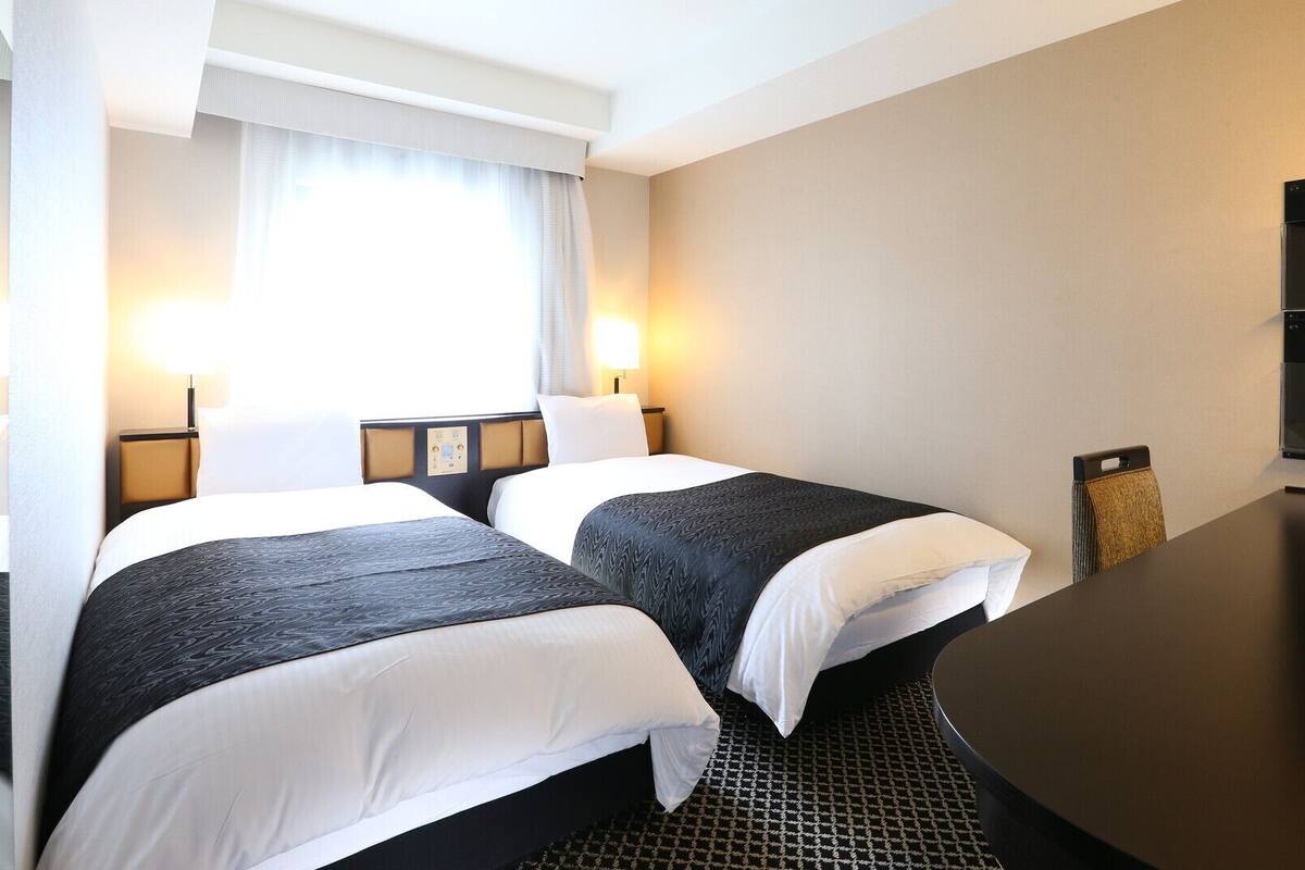 Una habitación de hotel con dos camas, un escritorio, una silla y un televisor.