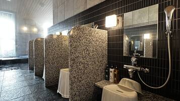 A modern bathroom with a black tiled wall, a mirror, a sink, and a shower area.