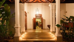 Una entrada bien iluminada con un camino de piedra que conduce a una puerta de madera, flanqueada por columnas blancas y plantas en macetas.
