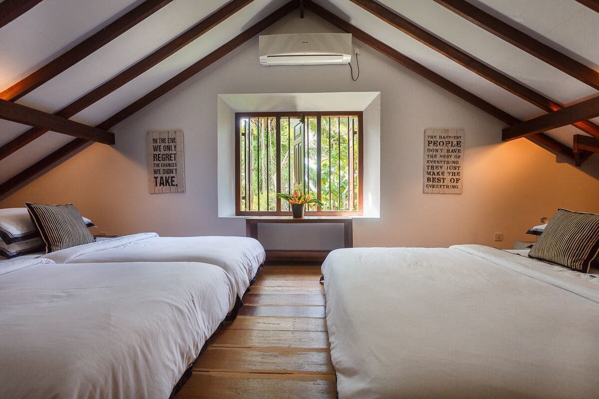Una habitación con dos camas, una ventana con persianas verticales y frases motivacionales en las paredes.
