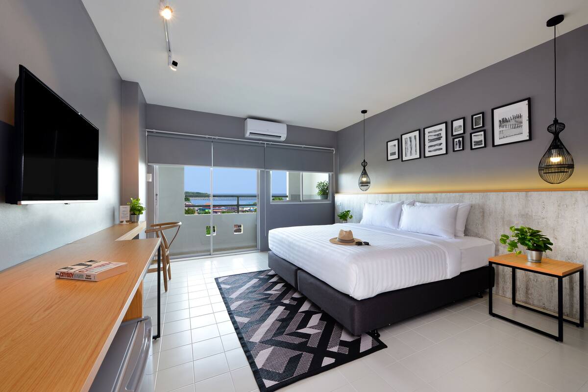 Un dormitorio moderno con cama, escritorio, televisor y balcón con vistas.
