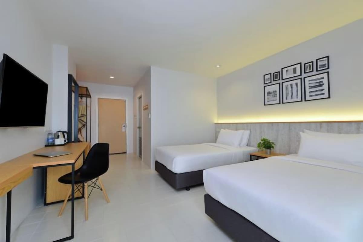A hotel room with a desk, two beds, a TV, and framed pictures on the wall.