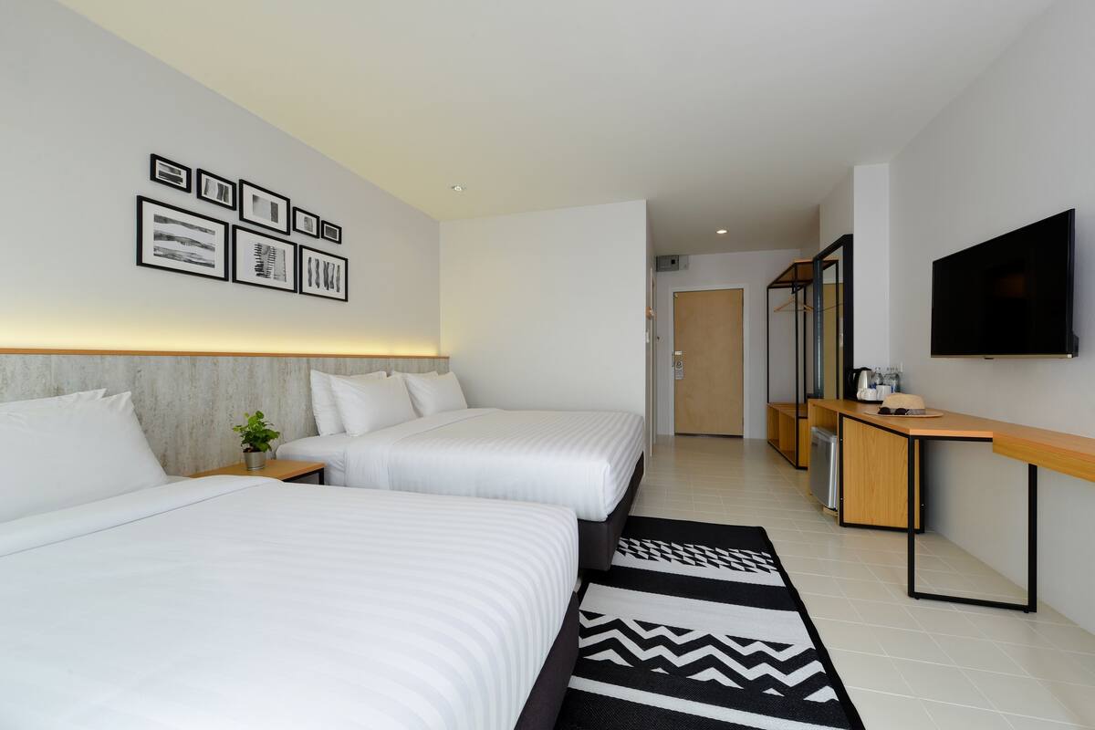 Una habitación de hotel con dos camas, un escritorio, un televisor y cuadros en la pared.