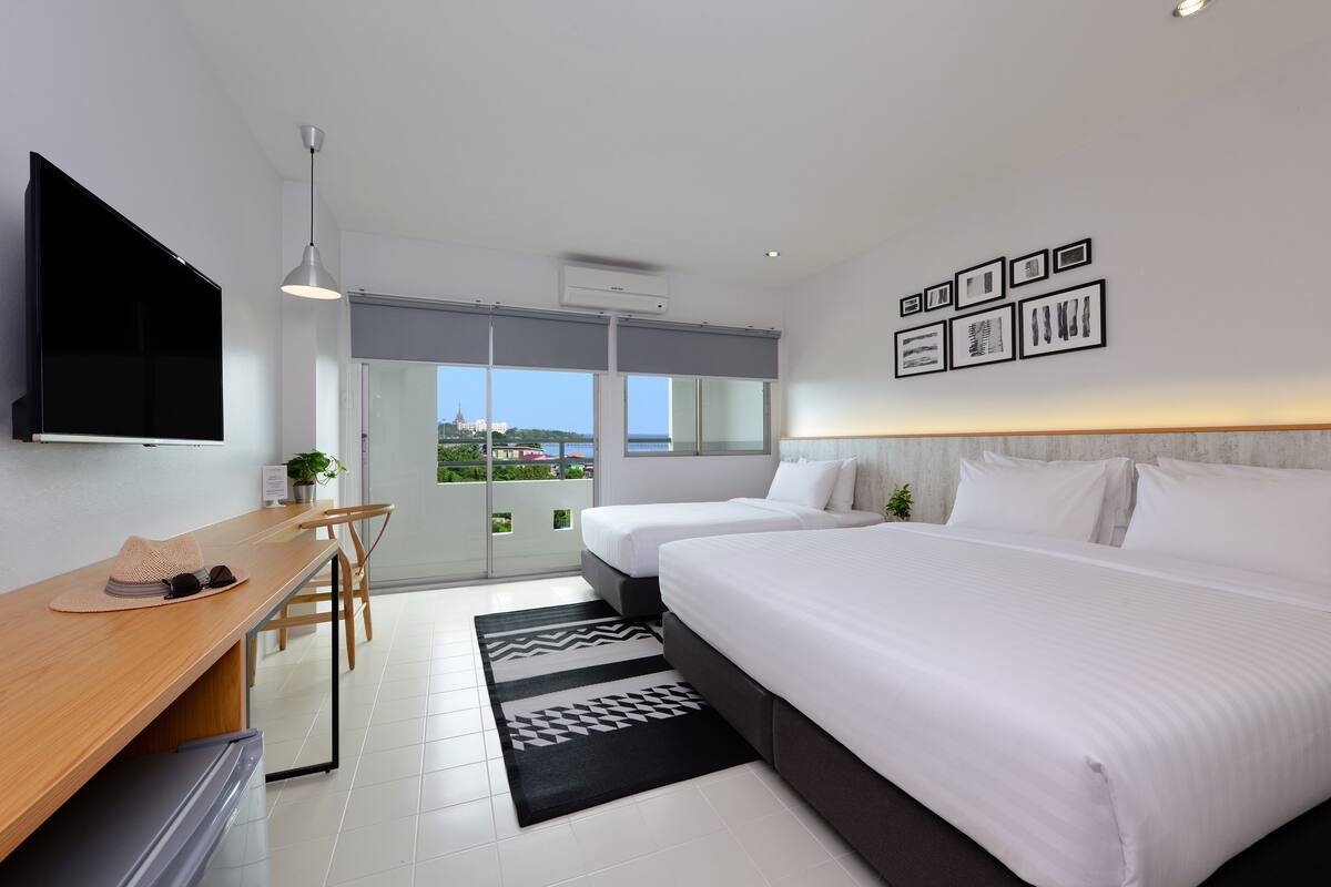 Una habitación de hotel moderna con una cama grande, un escritorio con televisor y vistas a la ciudad a través de amplias ventanas.
