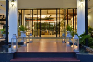 Uma entrada de hotel moderna com deck de madeira, portas de vidro e plantas em vasos.