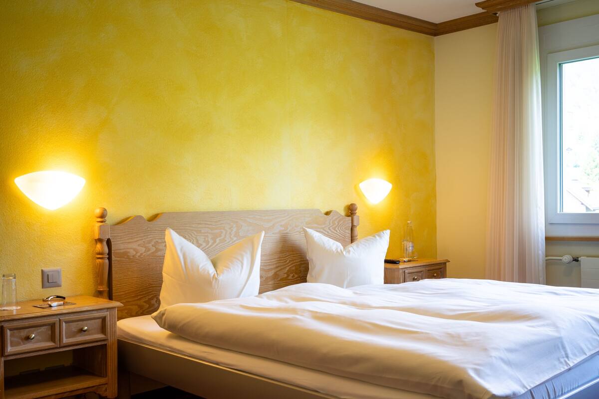 Quarto de hotel com uma cama grande, duas mesas de cabeceira e uma mesinha de apoio.