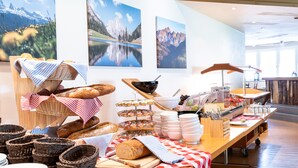 Un buffet proposant du pain, des viennoiseries et du fromage, avec une vue sur les montagnes en arrière-plan.