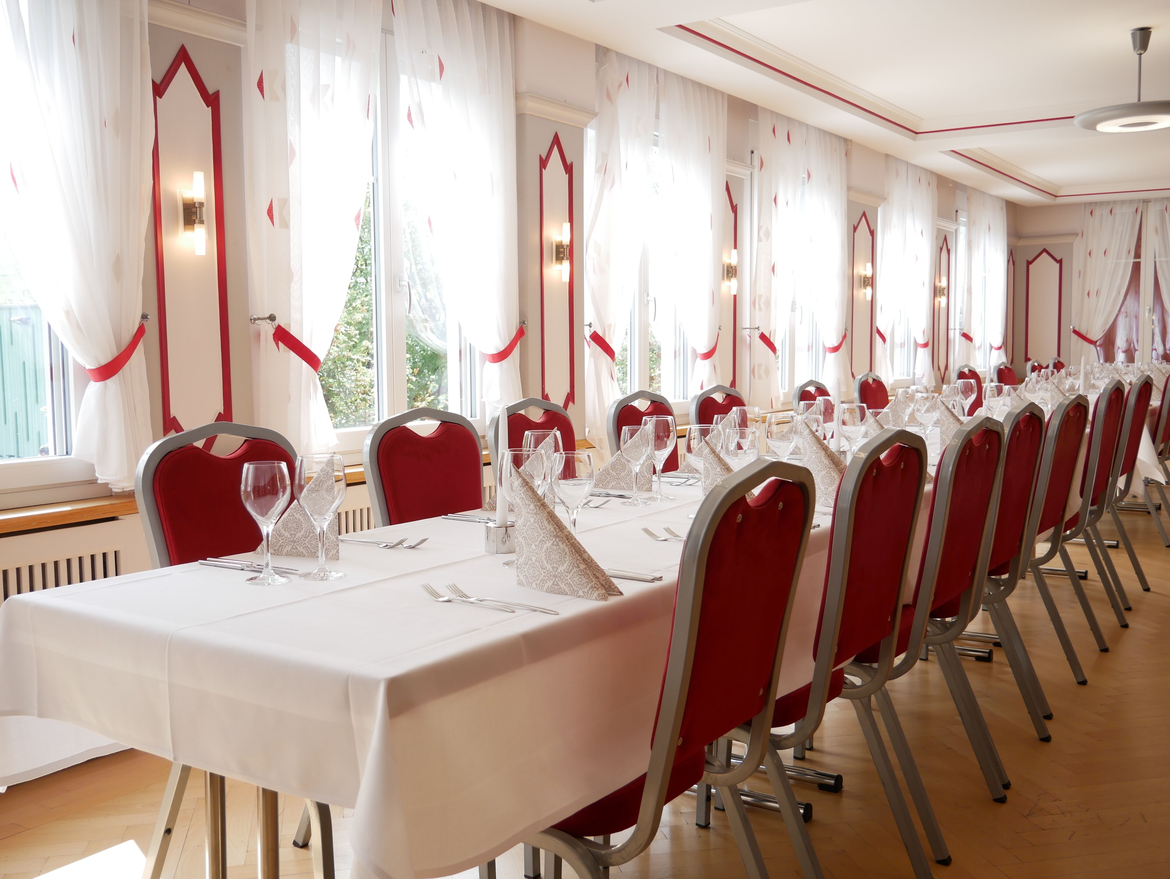 Une salle de banquet avec de longues tables, des chaises rouges et des nappes blanches.