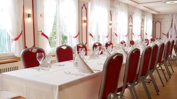 Une salle de banquet avec de longues tables, des chaises rouges et des nappes blanches.