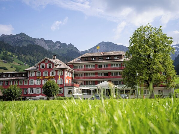 A hotel with multiple floors, a red facade, and a mountain backdrop.