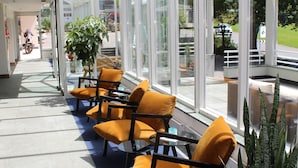 Une véranda aux murs de verre, un coin salon avec des chaises jaunes et un panneau indiquant la présence d’un restaurant.