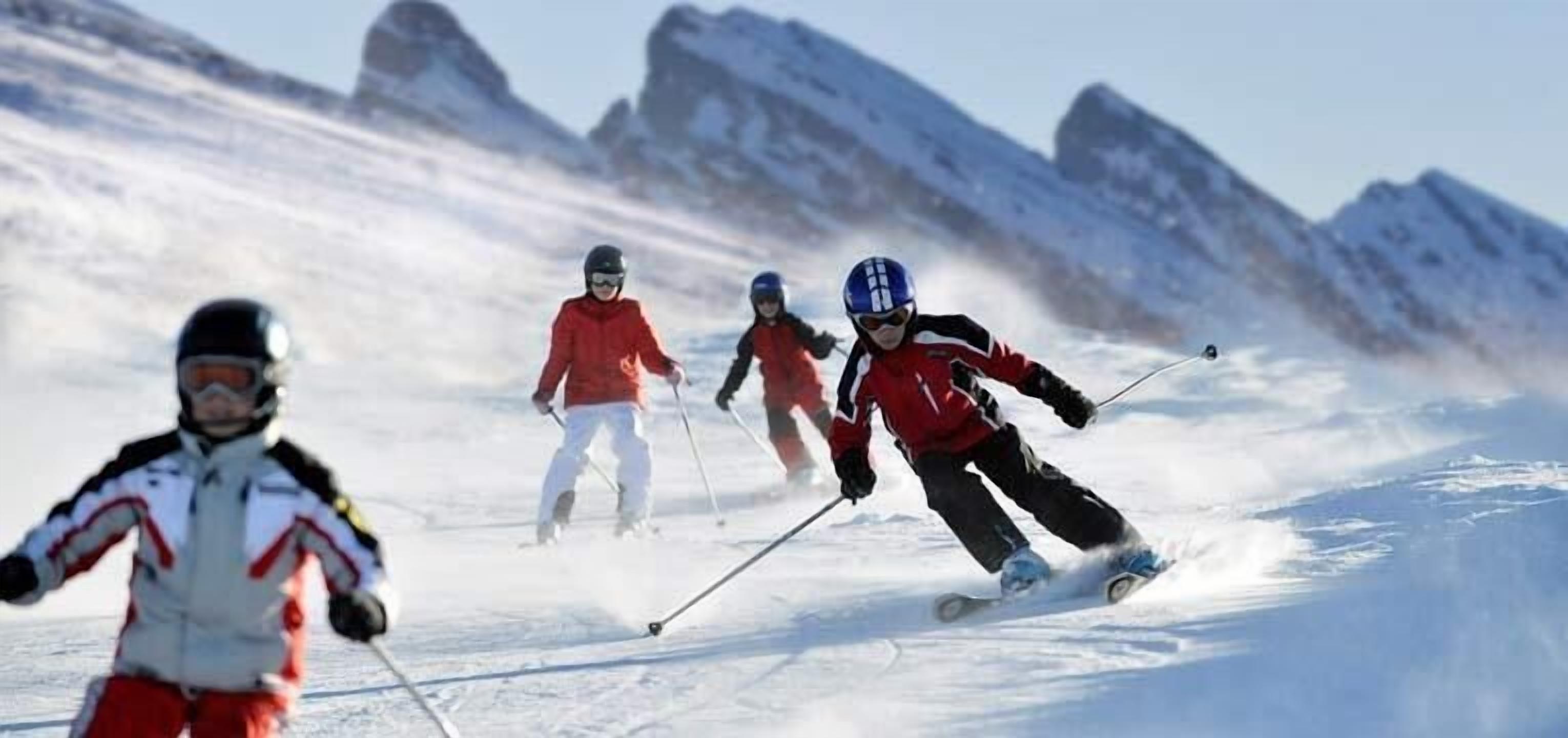 A group of skiers on a snowy slope with mountains in the background.