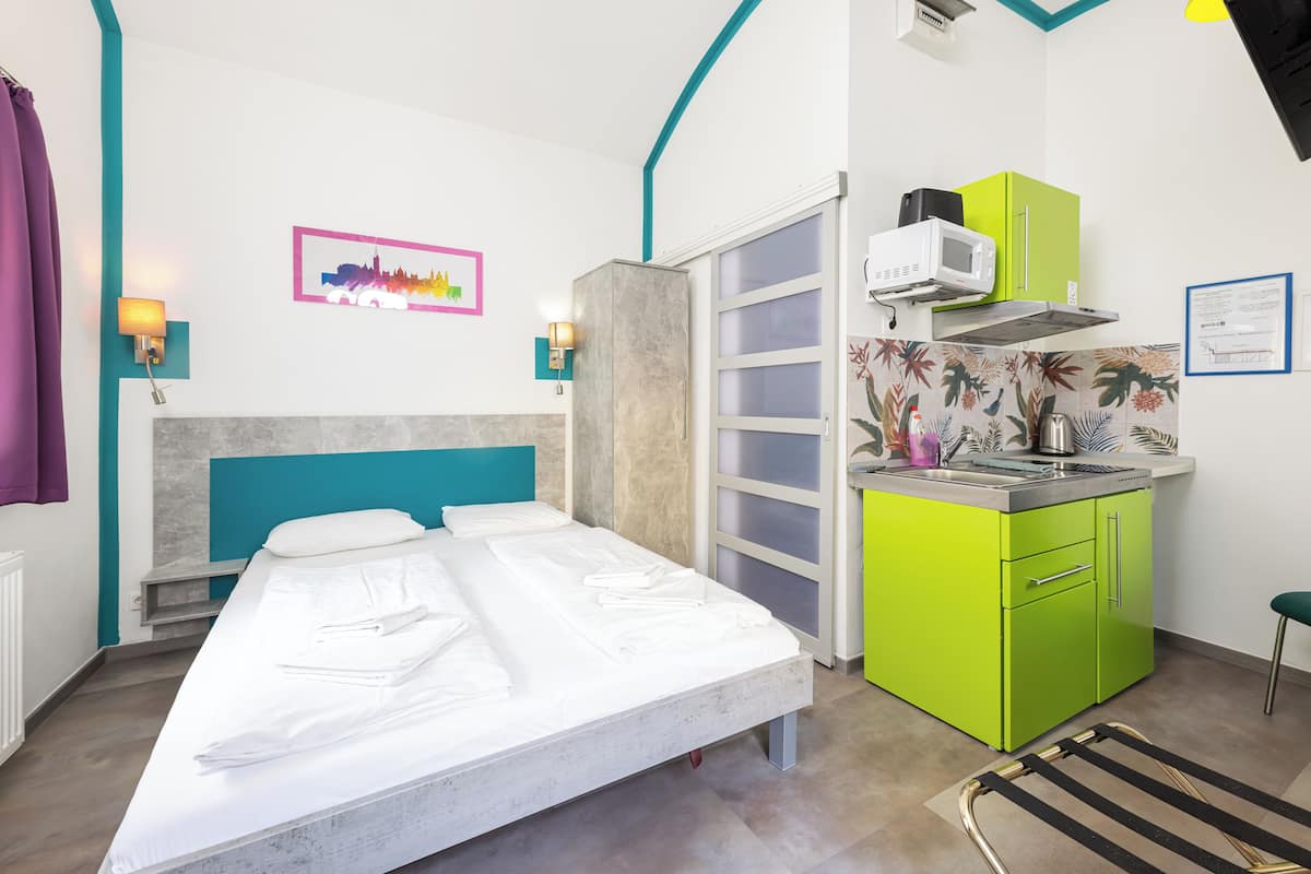 A compact hotel room with a bed, a kitchenette, and a bathroom.