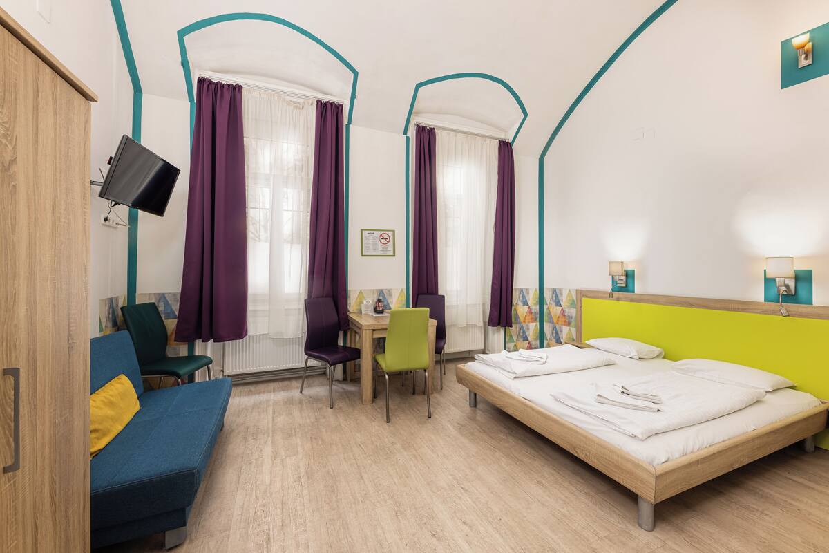 A hotel room with a bed, a desk, a chair, a sofa, and a TV.