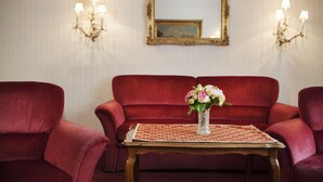 Een kamer met een rode bank, een kleine tafel met een bloevas, en wandlampen.