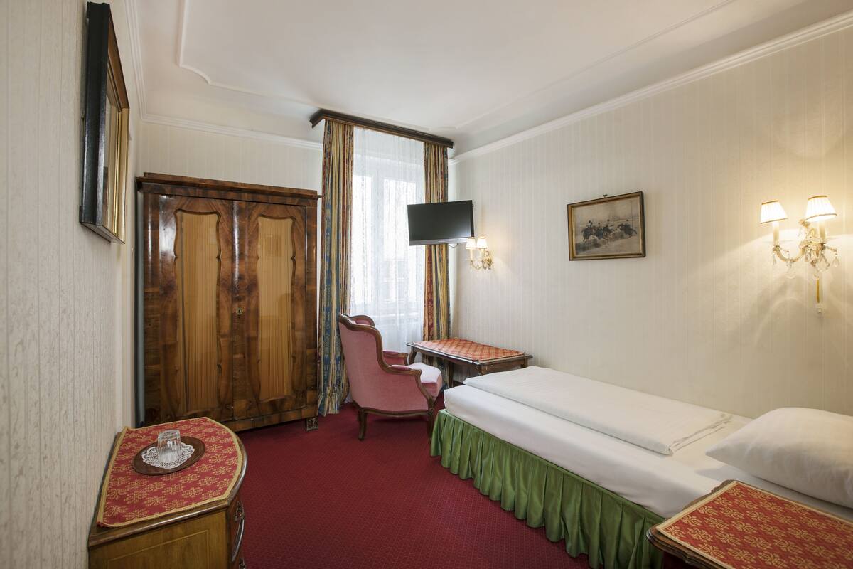 A hotel room with a bed, a desk, a chair, a television, and a wardrobe.