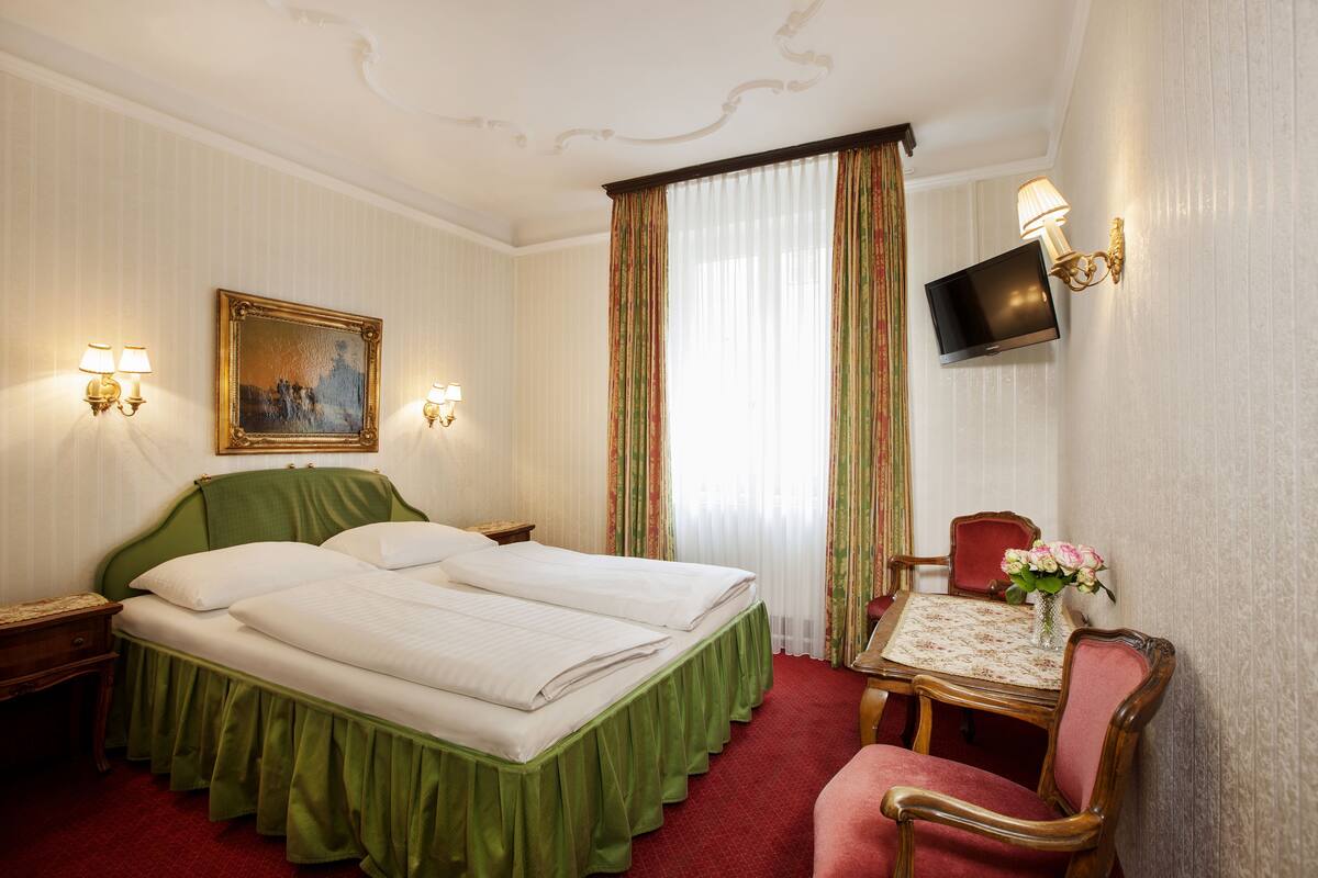 A hotel room with a bed, a desk, a chair, a television, and a painting on the wall.
