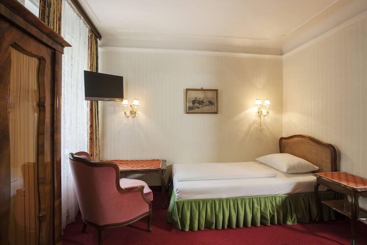 A hotel room with a bed, a desk, a chair, a television, and two wall-mounted lamps.