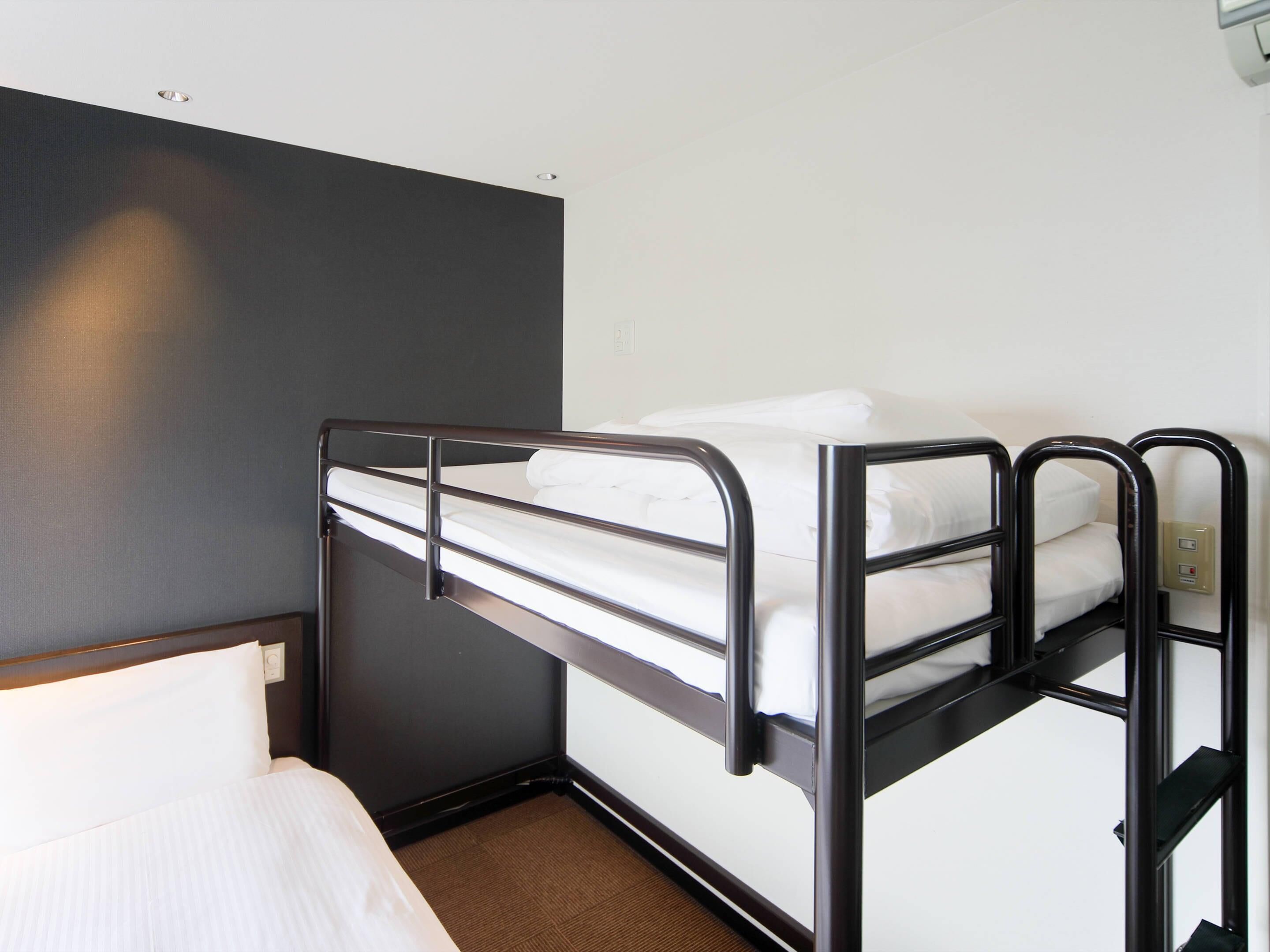 Una cama litera en una habitación de hotel con una pared lisa y una ventana pequeña.