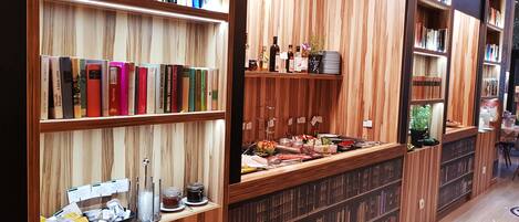 Une bibliothèque avec des étagères en bois remplies de livres et un coin café proposant diverses boissons et collations.