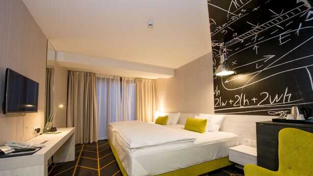 Une chambre d’hôtel avec un lit, un bureau, une chaise, un téléviseur et un mur couvert d’équations mathématiques.