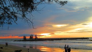 A beach scene with people, a pier, and a sunset. - Ajang Hotel (Miri)