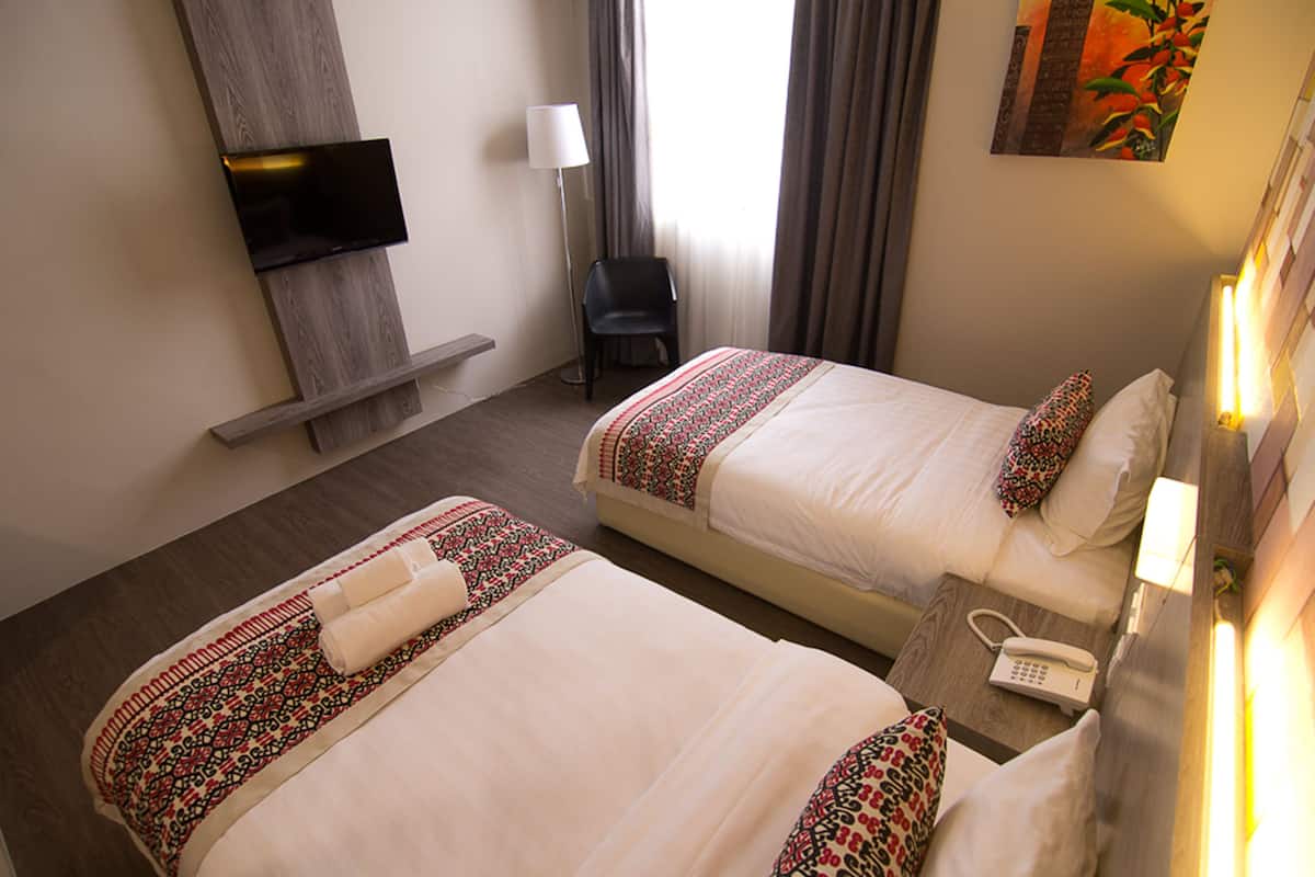 Hotellihuone, jossa on kaksi sänkyä, seinälle asennettu taulutelevisio, työpöytä puhelimineen ja tuoli.