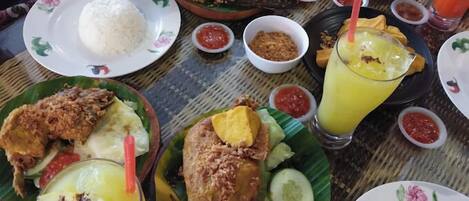 A table set with various dishes including fried fish, rice, and a yellow drink, likely a juice or smoothie.