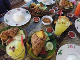 Una mesa servida con diversos platos, incluyendo pescado frito, arroz y una bebida amarilla, probablemente jugo o batido.