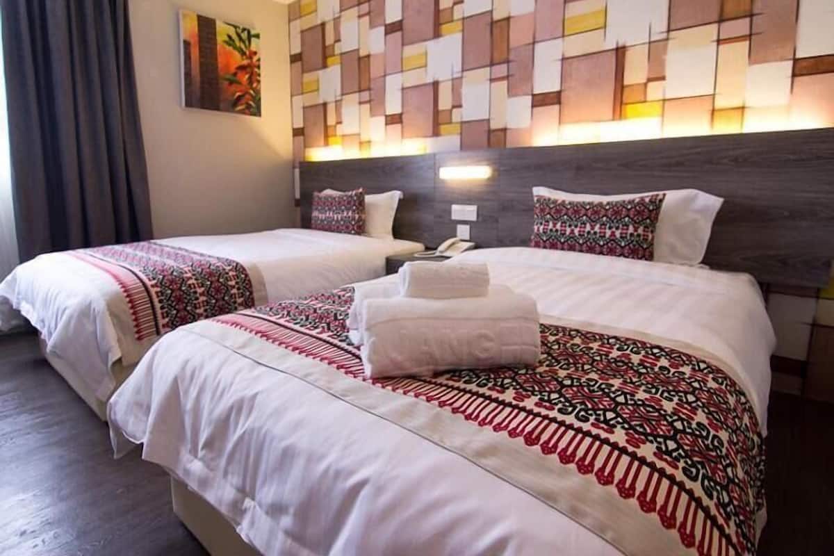 Hotellihuone, jossa on kaksi sänkyä, kuviollinen sängynpääty, taulu seinällä ja puhelin yöpöydällä.