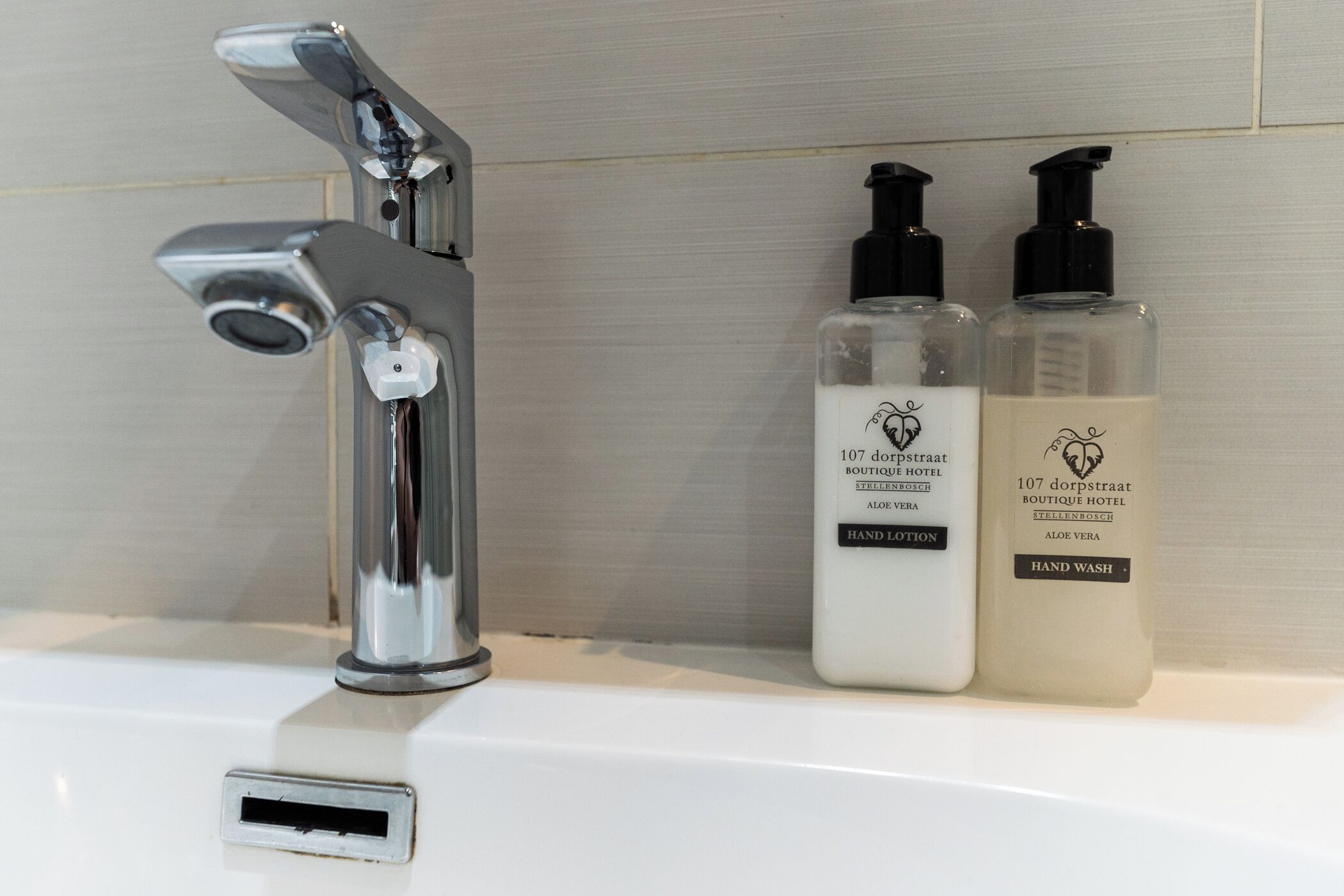 Ein Waschbecken mit chromfarbenem Wasserhahn und zwei Handseifenflaschen mit der Aufschrift '107 dorpstraat Boutique Hotel' und 'Aloe Vera'.