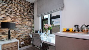 A modern kitchen with a stone wall, a window with a view, a dining area with a chair, and a coffee station.