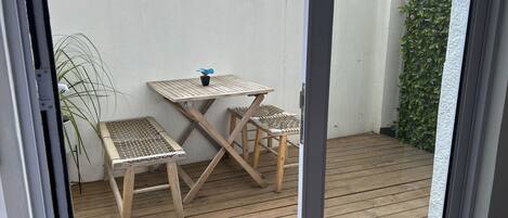 Une terrasse en bois avec une table et deux chaises, une plante en pot et un mur blanc.