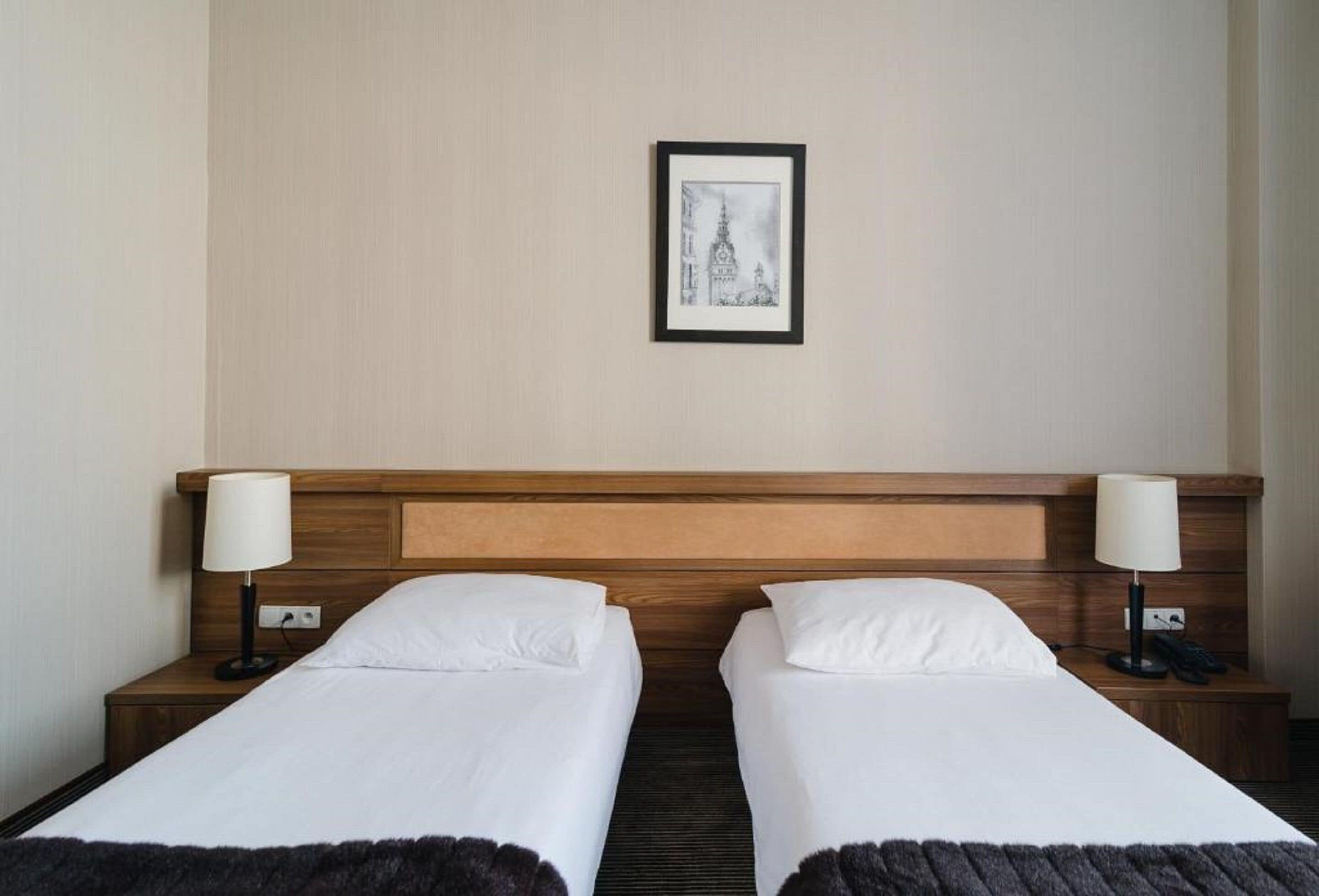 A hotel room with two single beds, wooden headboards, bedside lamps, and a framed picture on the wall.