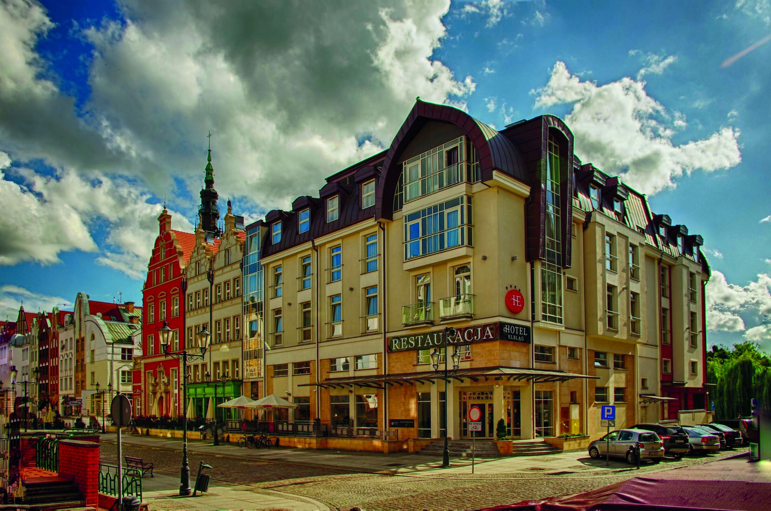 A hotel with a restaurant on the ground floor, a parking sign, and a street with cars.
