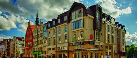 A hotel with a restaurant on the ground floor, a parking sign, and a street with cars.