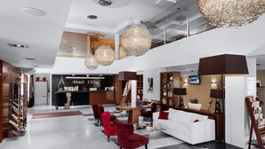 Un moderno vestíbulo de hotel con mostrador de recepción, zona de estar y una escalera que conduce a un nivel superior.
