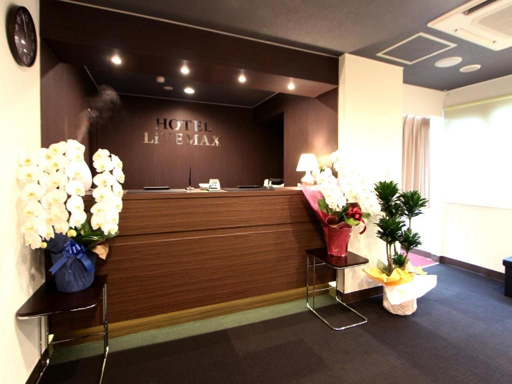 Una recepción de hotel con detalles en madera oscura, un reloj en la pared y un letrero que dice 'HOTEL L'INFIN MAX'.