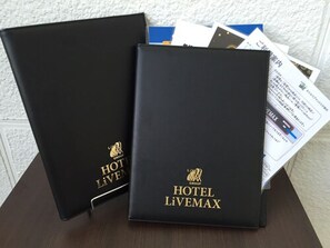 Dos carpetas negras con la marca 'HOTEL LIVEMAX' y un logo, sobre una mesa con algunos documentos.