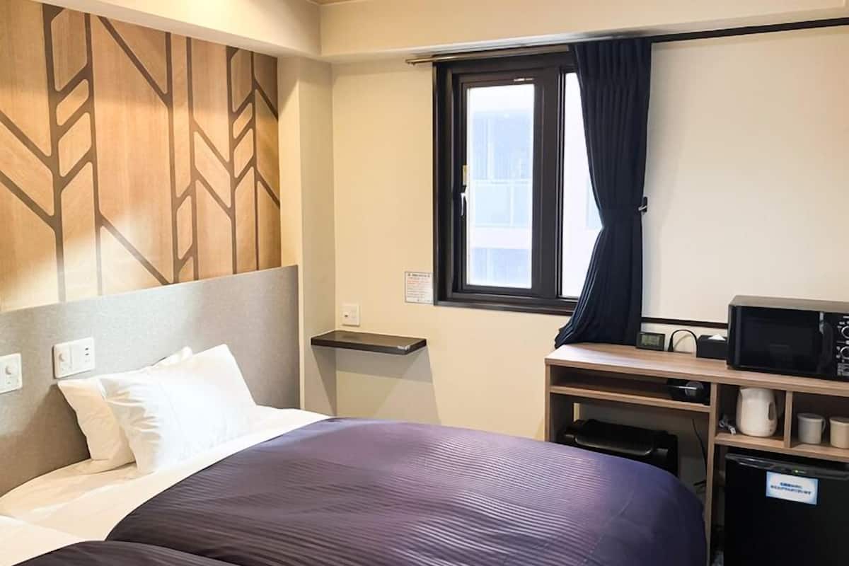 A hotel room with a bed, a desk with a computer, a microwave, and a small refrigerator.