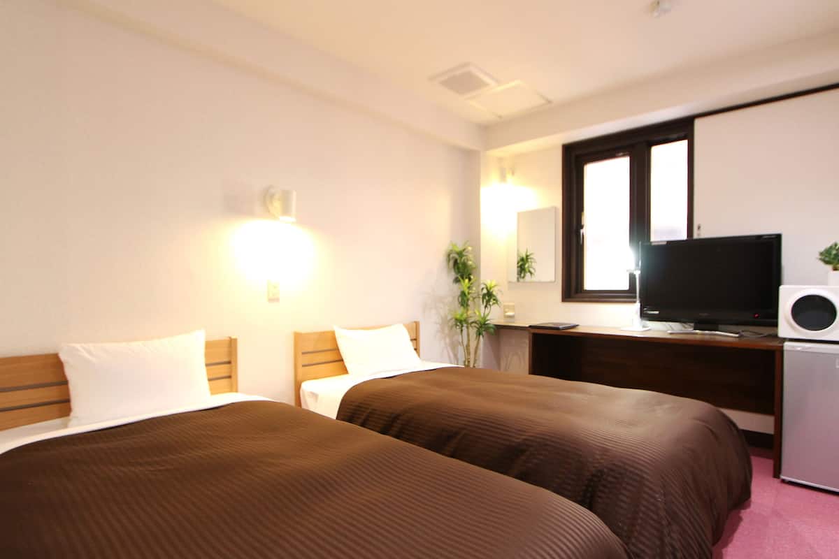 A hotel room with two beds, a desk with a computer and a television, and a small refrigerator.