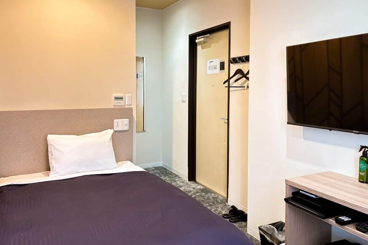 A hotel room with a bed, a TV, a mirror, a door, and a small desk with a bottle.