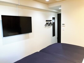 Una habitación con una cama, televisor montado y perchero con ganchos.