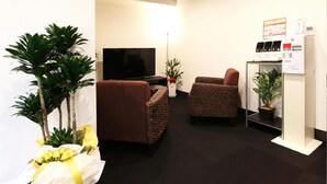 A living room with a flat-screen TV, two brown armchairs, a sofa, and a small plant on a stand. - Hotel Livemax Kita Fuchu (Fuchu)