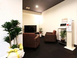 A living room with a flat-screen TV, two brown armchairs, a sofa, and a small plant on a stand.