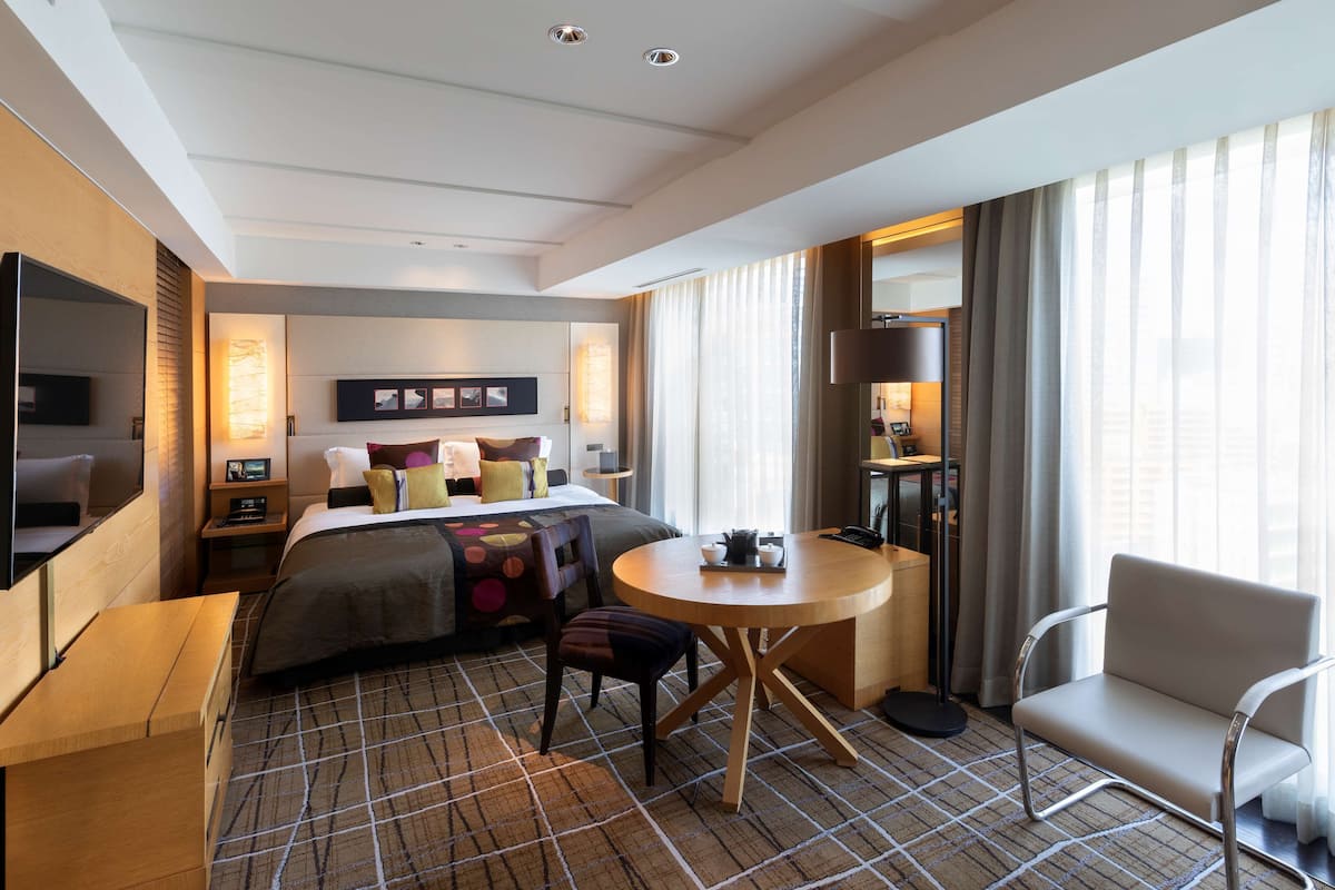 A hotel room with a bed, a desk, a chair, a round table, and a TV.