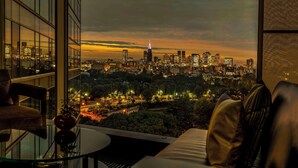 Una sala de estar moderna con una mesa de vidrio, un sofá y vistas a un horizonte urbano al anochecer.