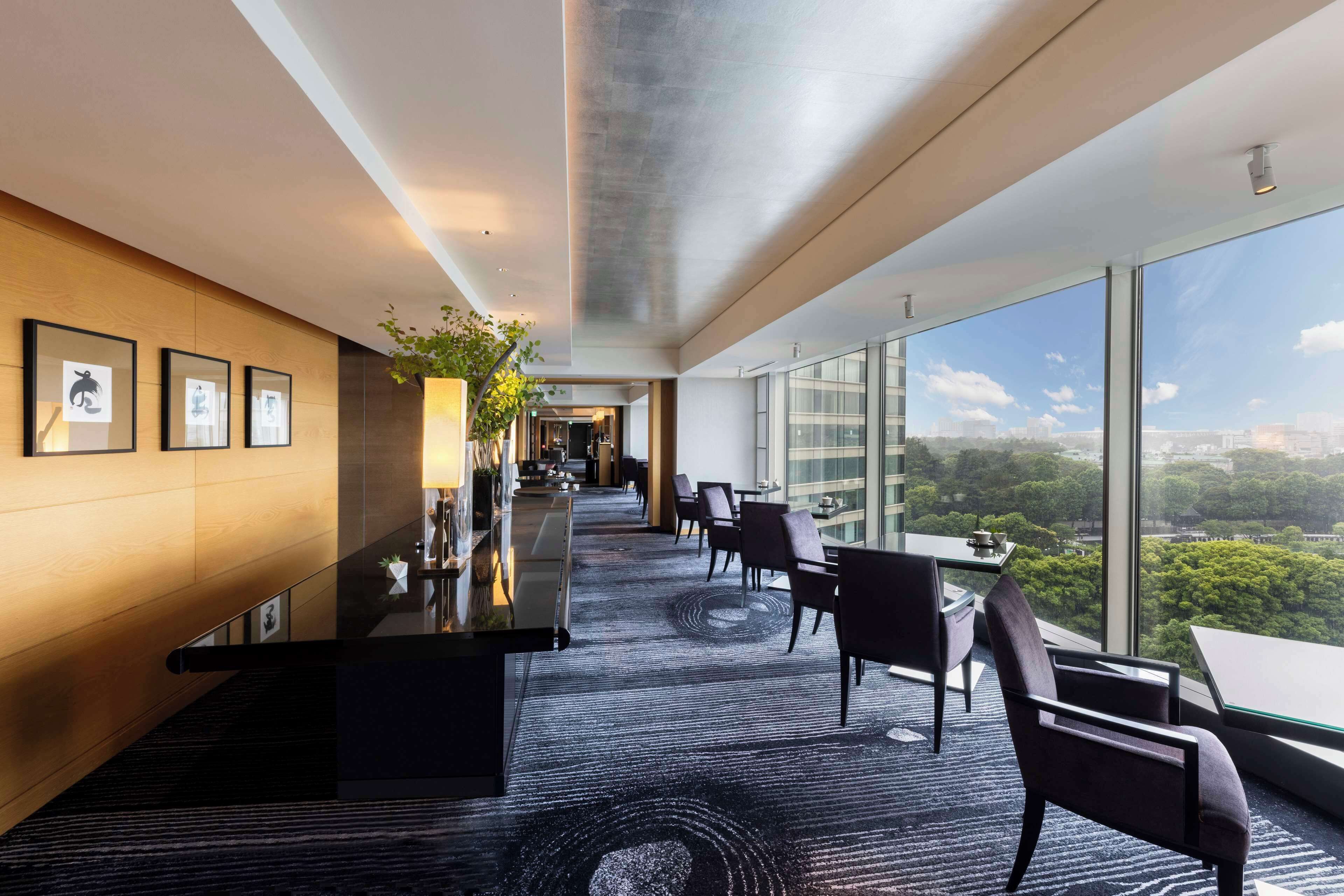 A modern hotel lobby with a long reception desk, seating area, and large windows offering a city view.