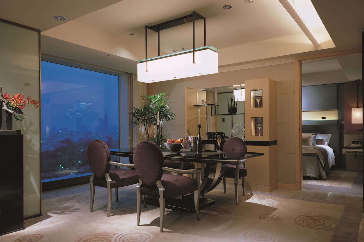 A modern dining area with a glass table, purple chairs, and a city view.